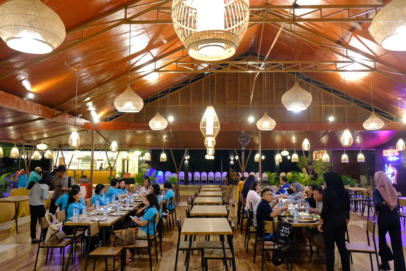Aula makan beratap kayu dengan deretan lampu rotan dan meja panjang