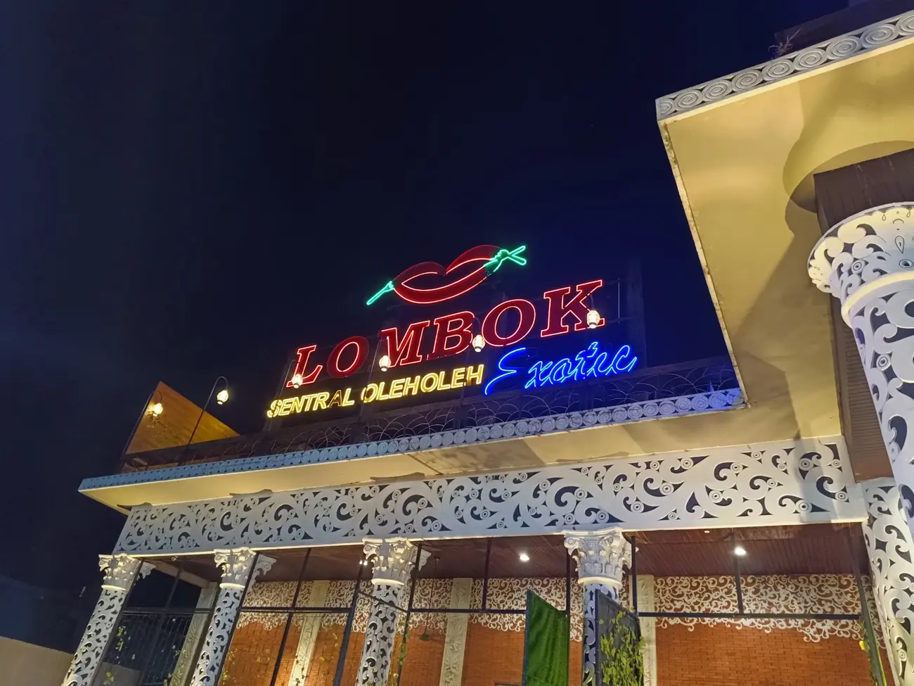 Gedung Lombok Exotic pada senja hari dengan papan neon menyala di atas barisan tiang