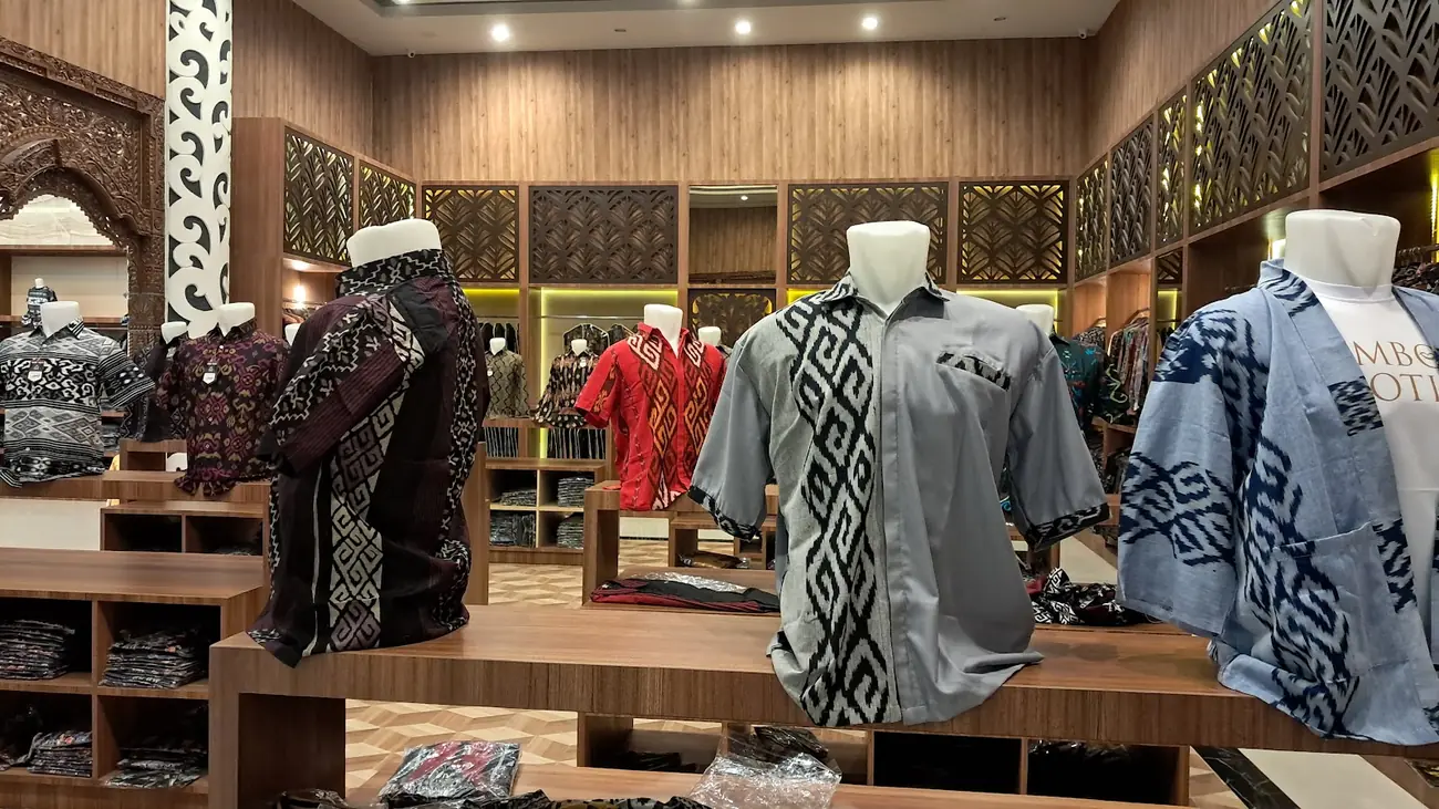 Manekin berbaju batik di antara rak kayu berisi busana bermotif